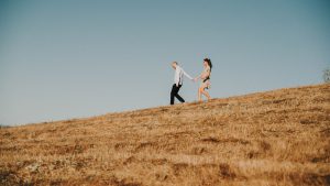 man leading woman down grassy hill