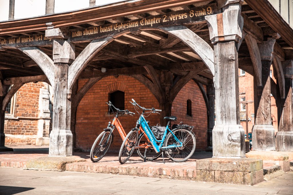 Two e-bikes parked underneath an old town hall in a town centre, Market Harborough, Leicestershire. For cycling, e-bikes, commuting, and communities.