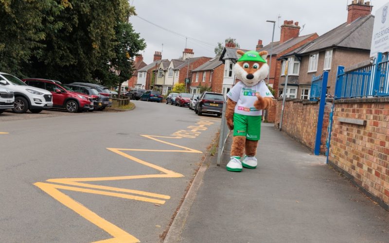Choose How You Move's fox mascot walking on a path next to a school and zig zag lines