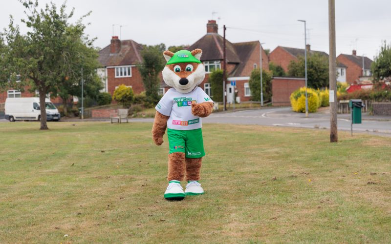 Theo the Fox, the Choose How You Move schools' mascot, walking across a park in a Leicestershire village