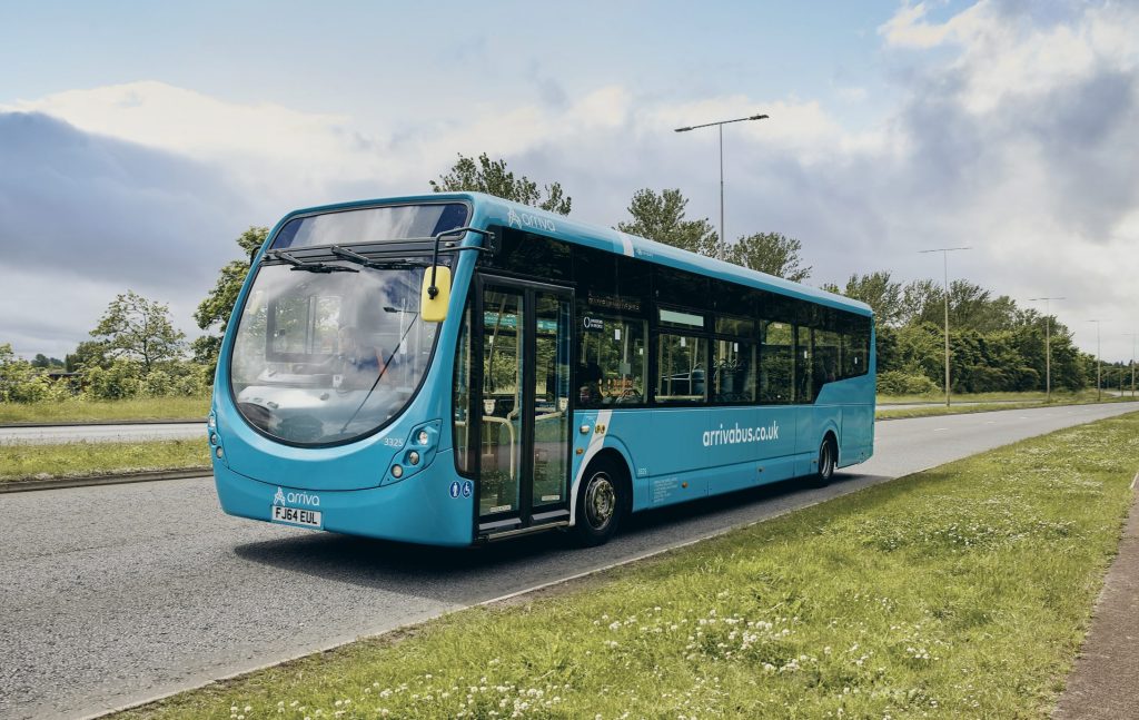 Arriva bus driving on a road with grass verges either side of the road. 