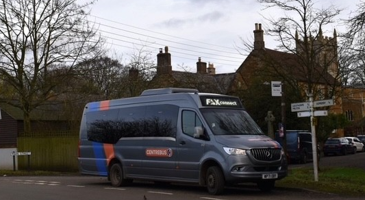 Grey FoxConnect minibus at a bus stop in a rural town