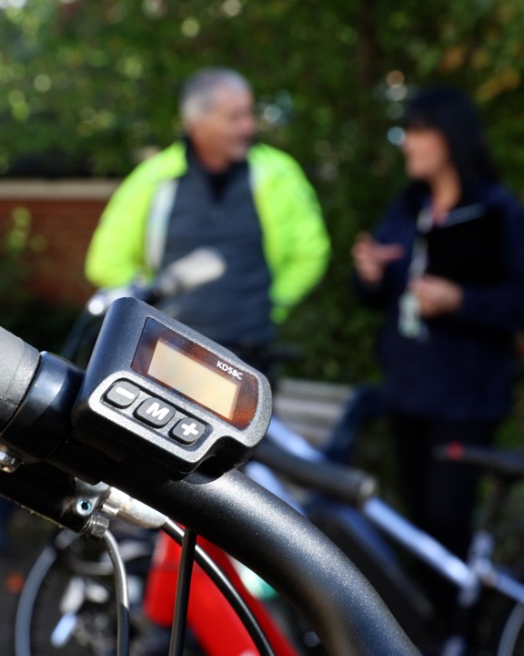 Two people talking in the background with the focus on the handlebars of an e-bike