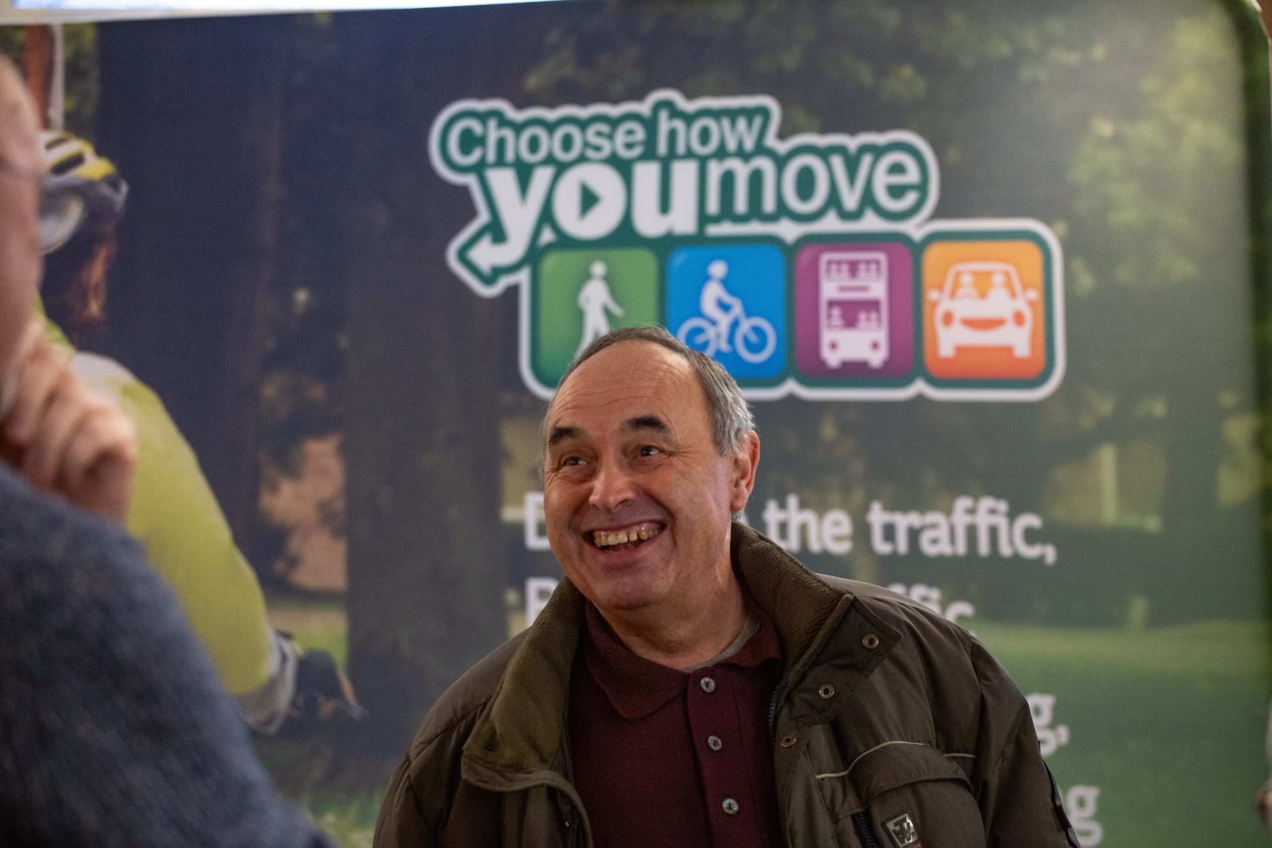 Person having a conversation and smiling in front of a Choose How You Move-branded sign at the Cycling, Walking and Wheeling Forum
