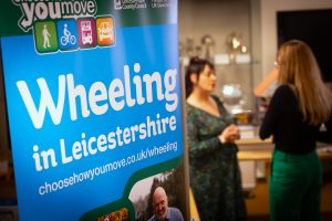Two women speaking with a Wheeling in Leicestershire sign in front