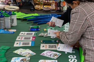 People discussing routes on a Choose How You Move stall, with maps, pencils, bags, umbrellas, and leaflets spread out on the table. For communities and business engagement.