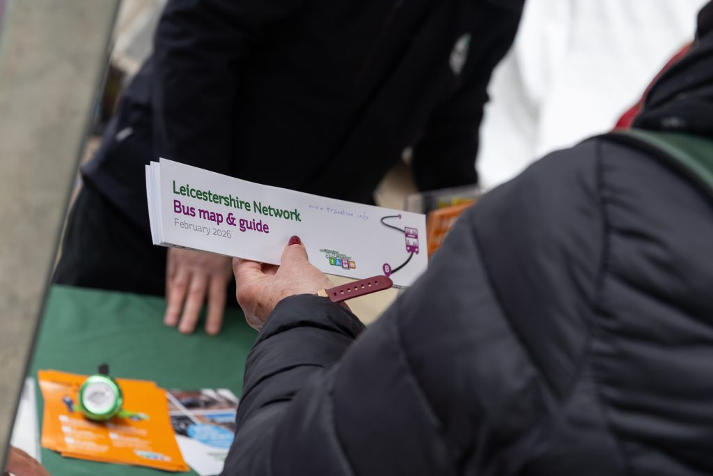A person holding a bus map and guide leaflet at a stall. For businesses, Leicestershire business programme, communities, public transport.
