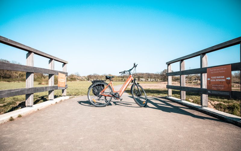 an orange electric bike parked on a footpath bridge on a sunny day. For information on e-bikes and electric bikes.