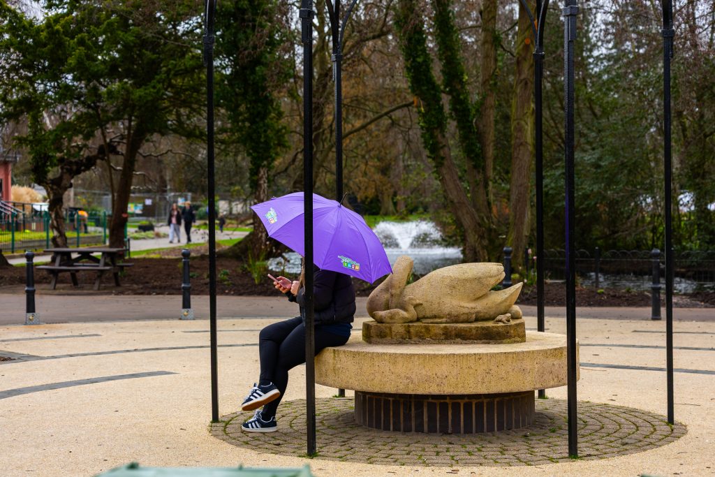 person with a Choose How You Move umbrella sitting at a fountain and reading from their phone
