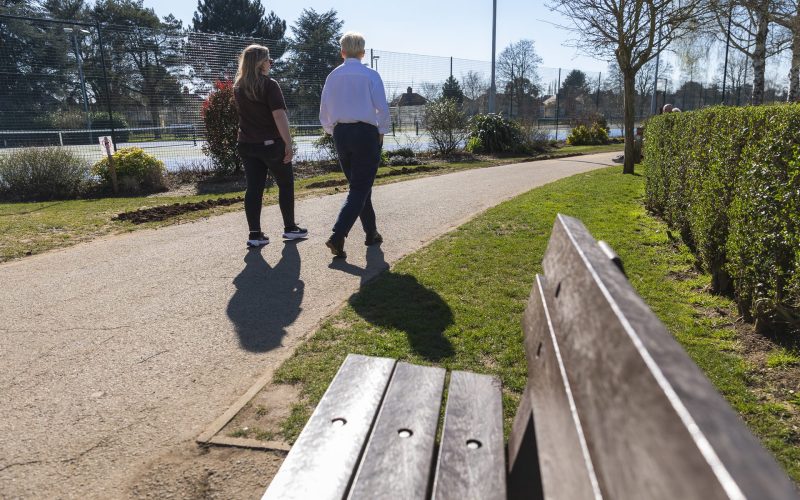two people walking past a bench in a park