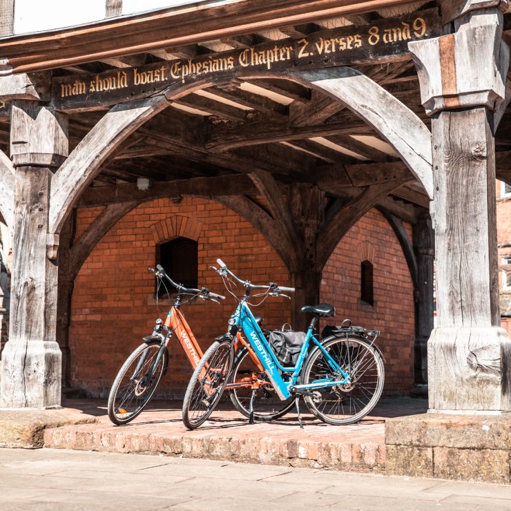 Two e-bikes parked underneath an old town hall in a town centre, Market Harborough, Leicestershire. For cycling, e-bikes, commuting, and communities.