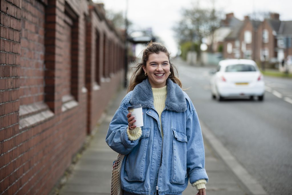 A woman in a blue jacket holding a coffee and walking to work. For commuting, Leicestershire Businesses, business programme.
