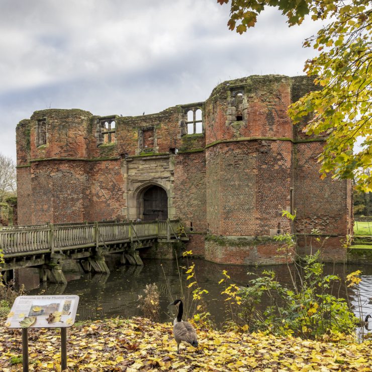 Kirby Muxloe Castle is an unfinished moated 15th century fortified manor house in Kirby Muxloe, Leicestershire, England, Uk A bridge on a moat leading up to Kirby Muxloe Castle, a ruined red-brick castle. On the bank, a goose walks amongst yellow leaves. For Blaby district.
