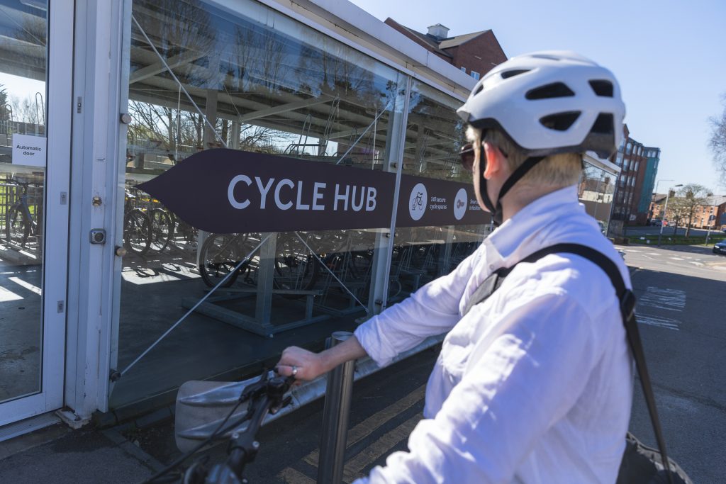 A person riding their bike in front of a Cycle Hub at a train station in Leicestershire. For cycling, commuting, Leicestershire businesses, new developments, communities.