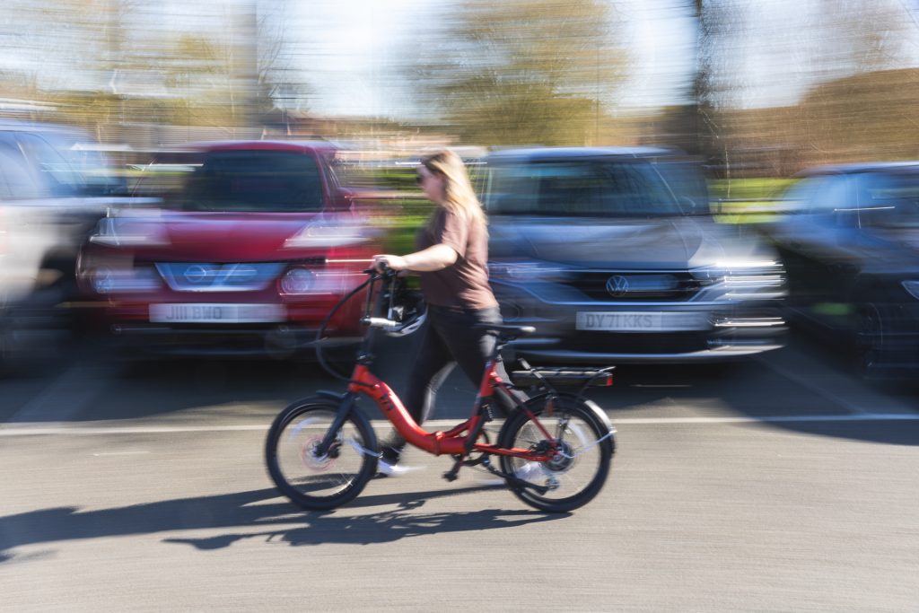 A person guiding a bike walking quickly past a row of cars. For walking, cycling, commuting, Leicestershire businesses business programme.