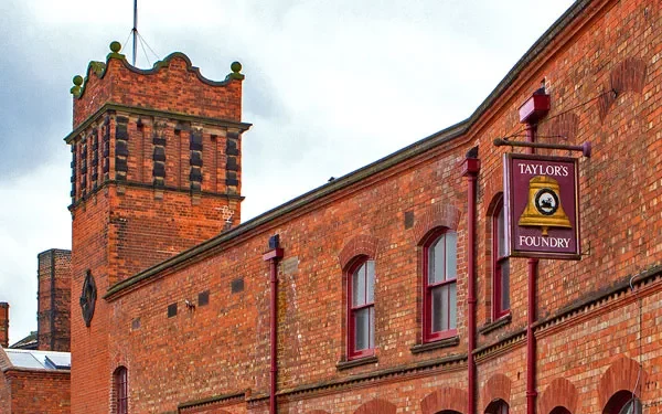 Historic red brick industrial building with arched windows and a sign reading 'Taylors Foundry