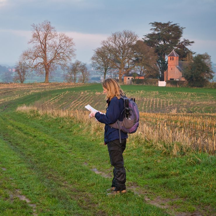A single woman walker in walking gear on a route through a cut field of crop stubble checks her route with a map. A single woman walker in walking gear on a route through a cut field of crop stubble checks her route with a map. A volunteer for communities work.