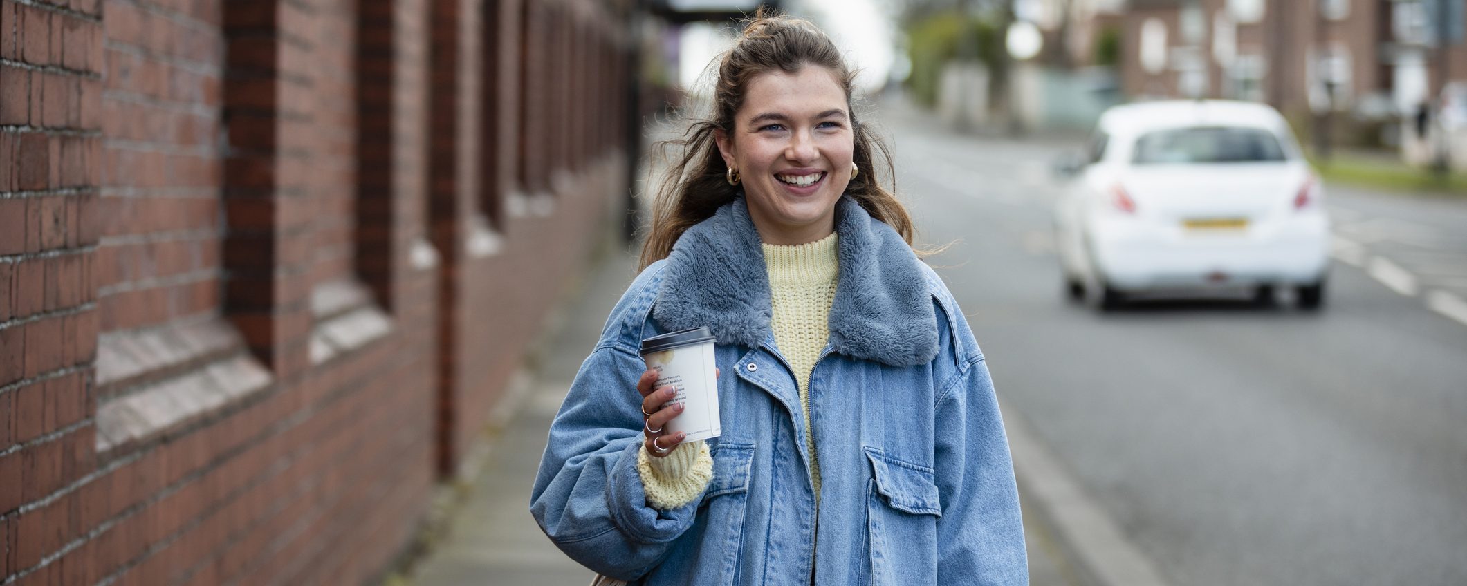 A woman in a blue jacket holding a coffee and walking to work. For commuting, Leicestershire Businesses, business programme.