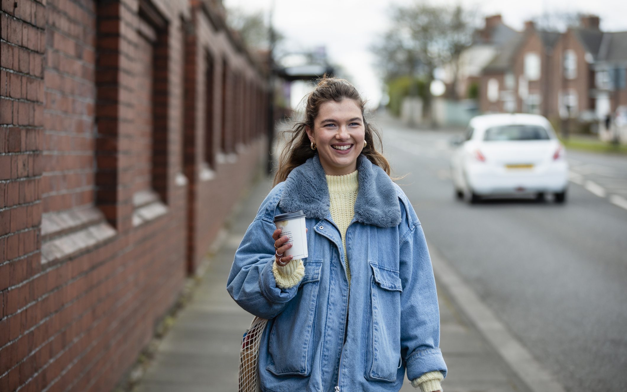 A woman in a blue jacket holding a coffee and walking to work. For commuting, Leicestershire Businesses, business programme.