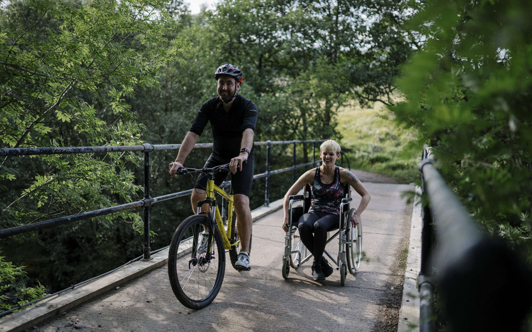 Couple exercising together on a bicycle and in a wheelchair.