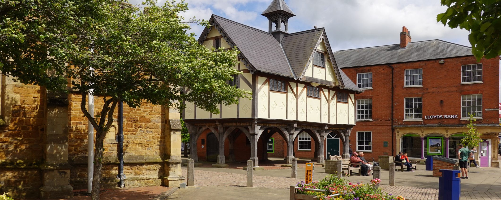 An old market hall in a paved square in in Market Harborough, with wooden arches and Tudor detailing.