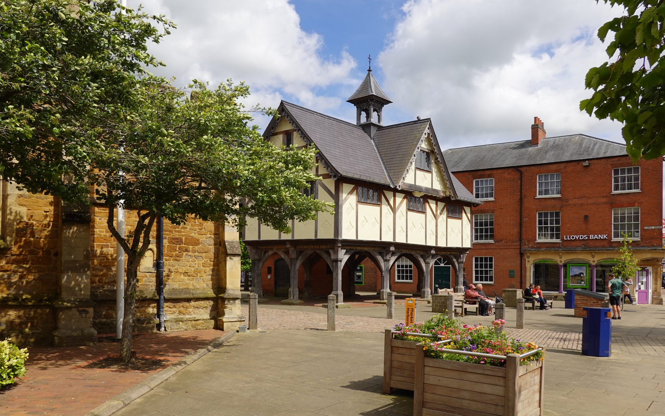 An old market hall in a paved square in in Market Harborough, with wooden arches and Tudor detailing.