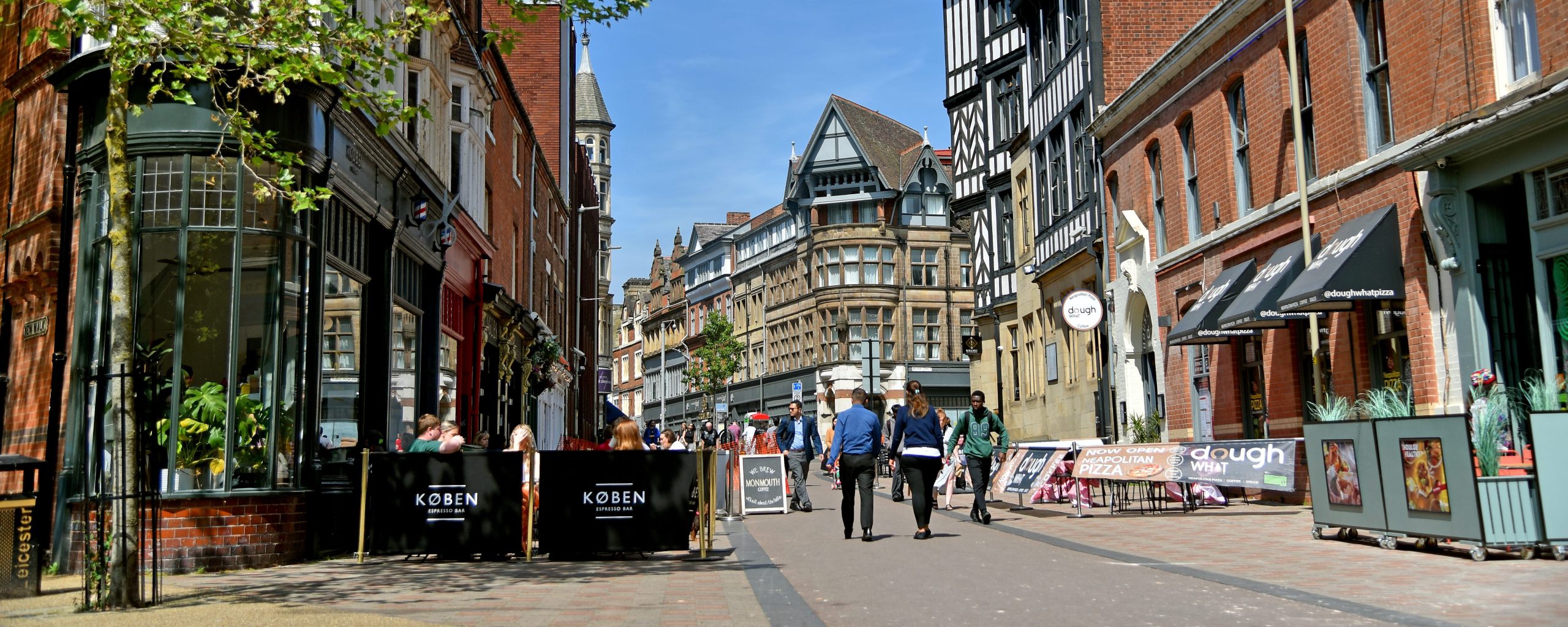 A paved path in Leicester city centre that people re walking down, with shops and public information signage.