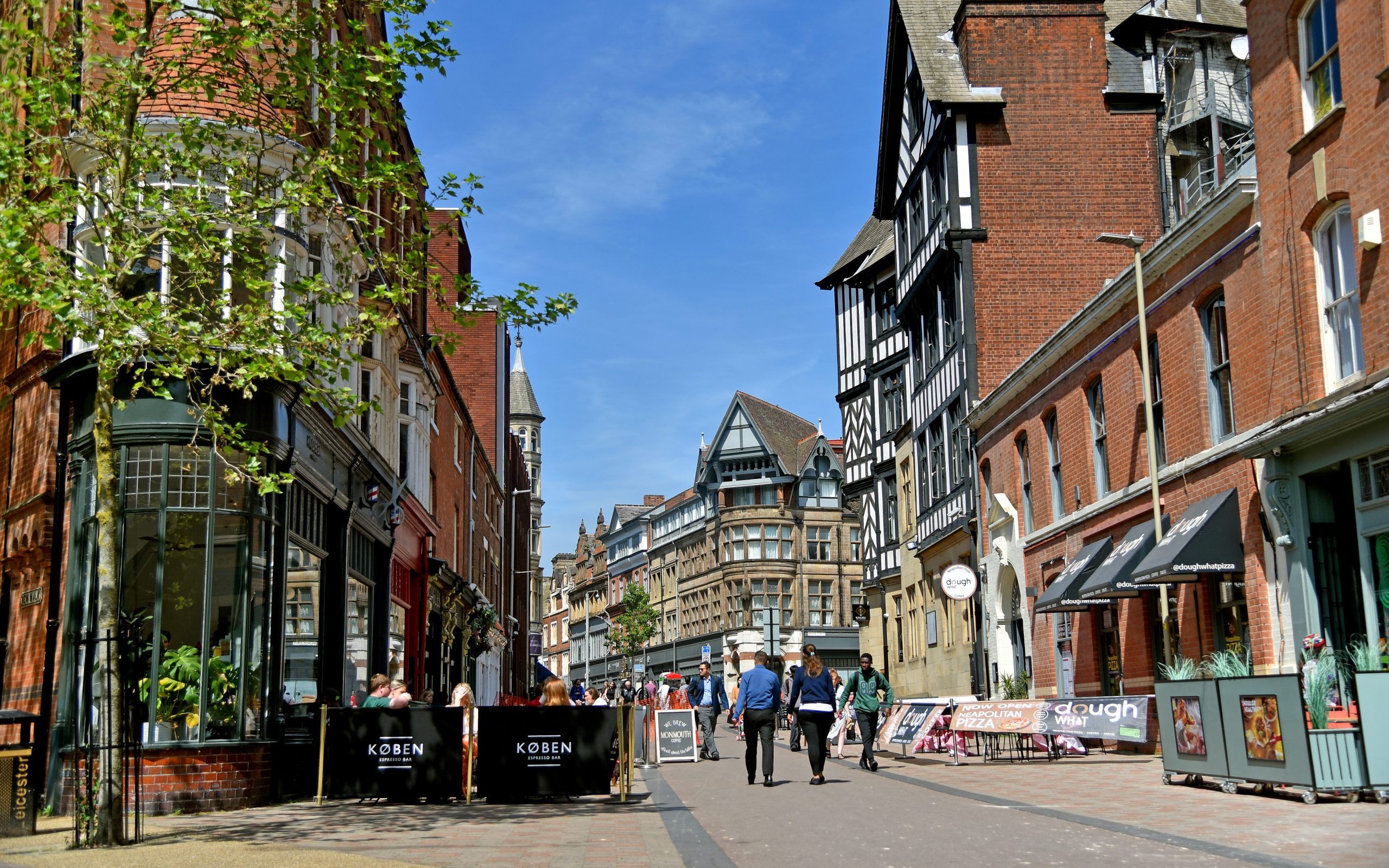 A paved path in Leicester city centre that people re walking down, with shops and public information signage.
