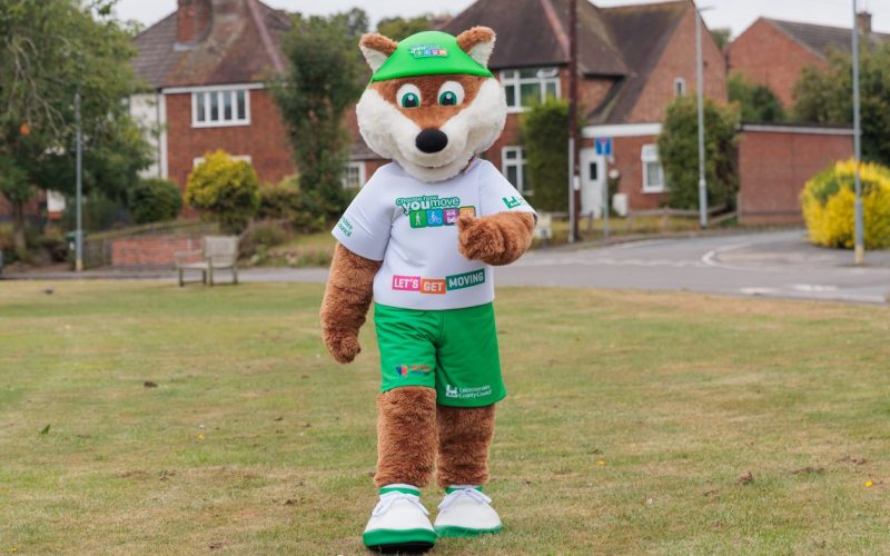 Theo the Fox, the Choose How You Move schools' mascot, walking across a park in a Leicestershire village