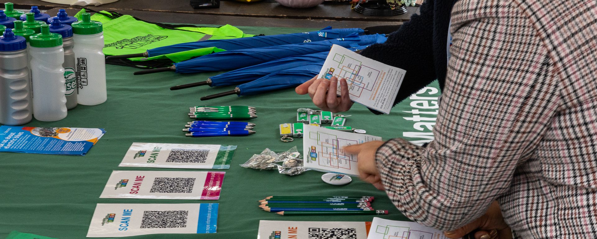 People discussing routes on a Choose How You Move stall, with maps, pencils, bags, umbrellas, and leaflets spread out on the table. For communities and business engagement.