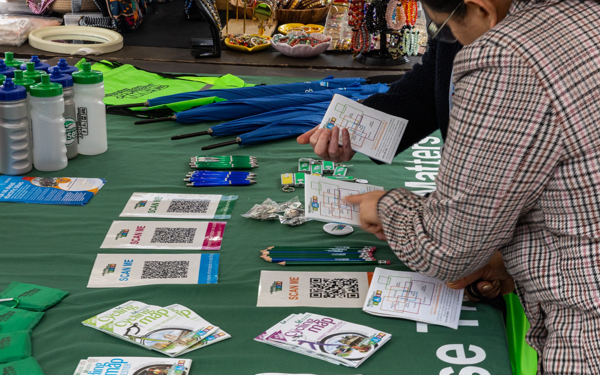 People discussing routes on a Choose How You Move stall, with maps, pencils, bags, umbrellas, and leaflets spread out on the table. For communities and business engagement.