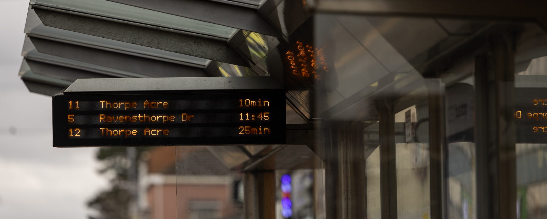 A digital real-time bus timetable listing three upcoming buses, fixed onto the roof of a bus stop.