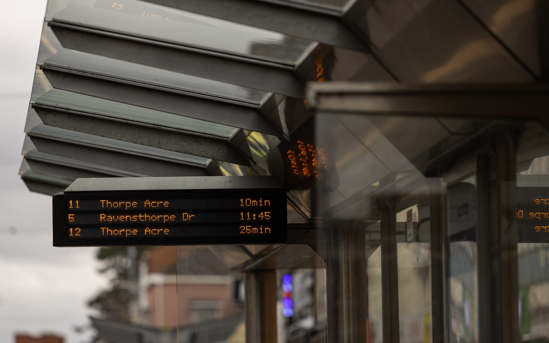 A digital real-time bus timetable listing three upcoming buses, fixed onto the roof of a bus stop.