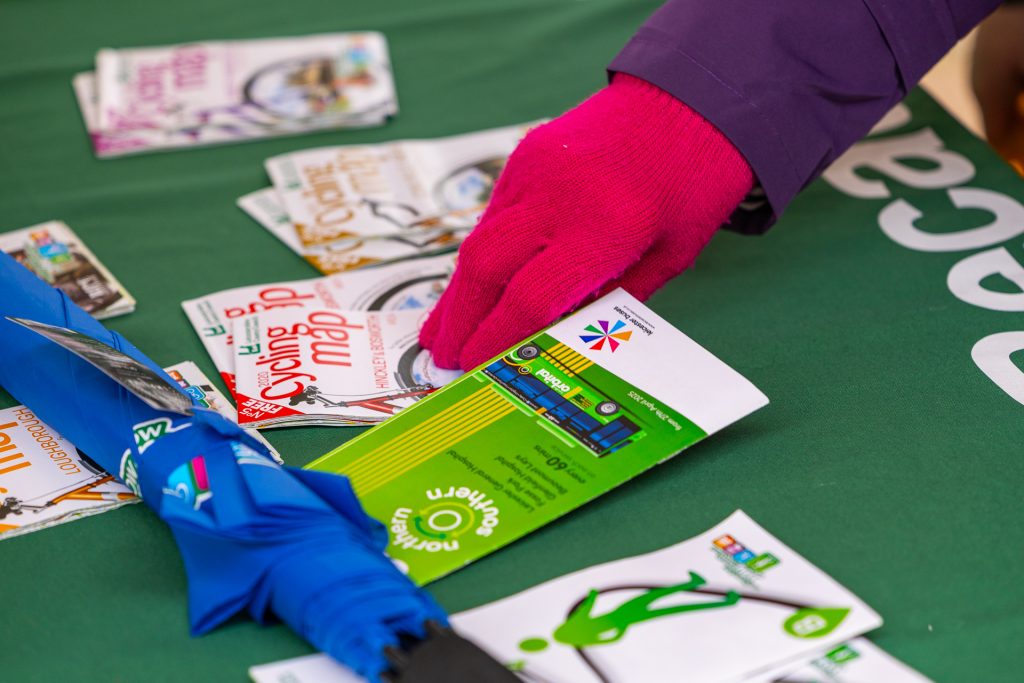 a person with red gloves picking up a leaflet from Choose How You Move - for communities roadshow