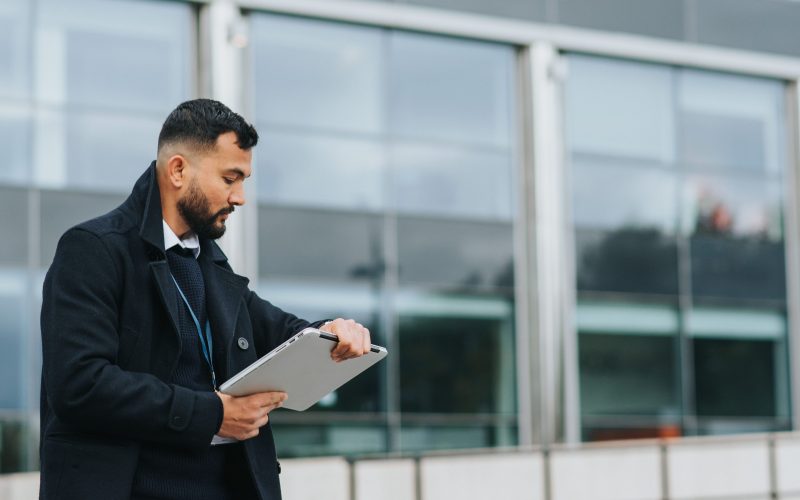 A man with a tablet outside a glass building, for businesses, Leicestershire business programme.
