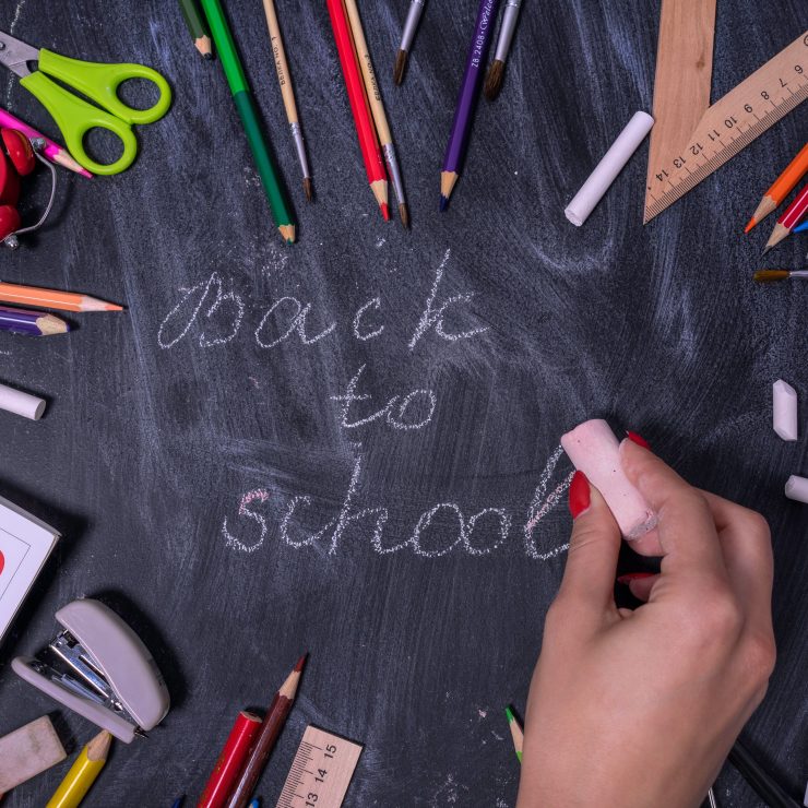 The words "Back to school" written on a chalkboard with scissors, pencils, rulers, planners and a rubber on top.
