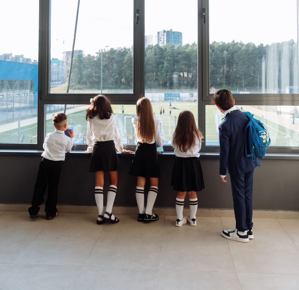 Four schoolchildren in uniform looking out onto a school playground - for schools