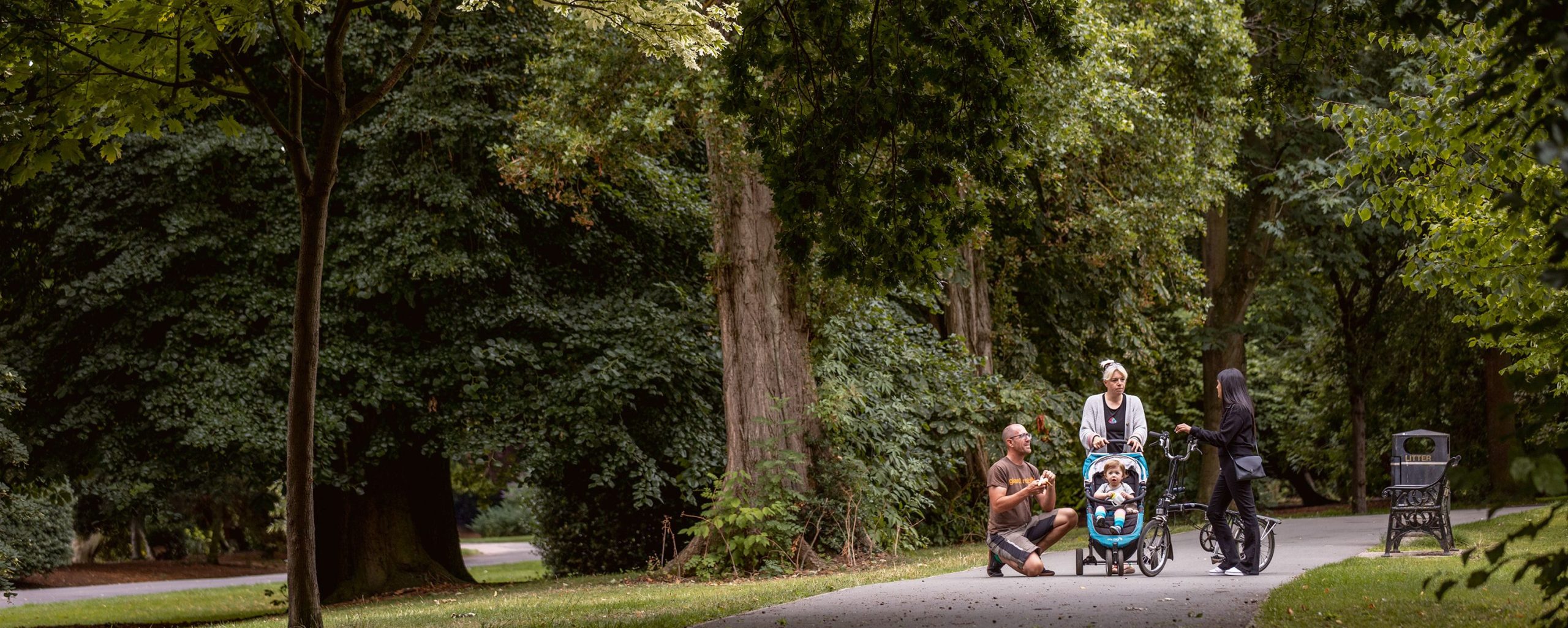 Two parents look after a small child in a pram, and talk to a woman using a bike on a path in Cycling and walking route in Leicester.