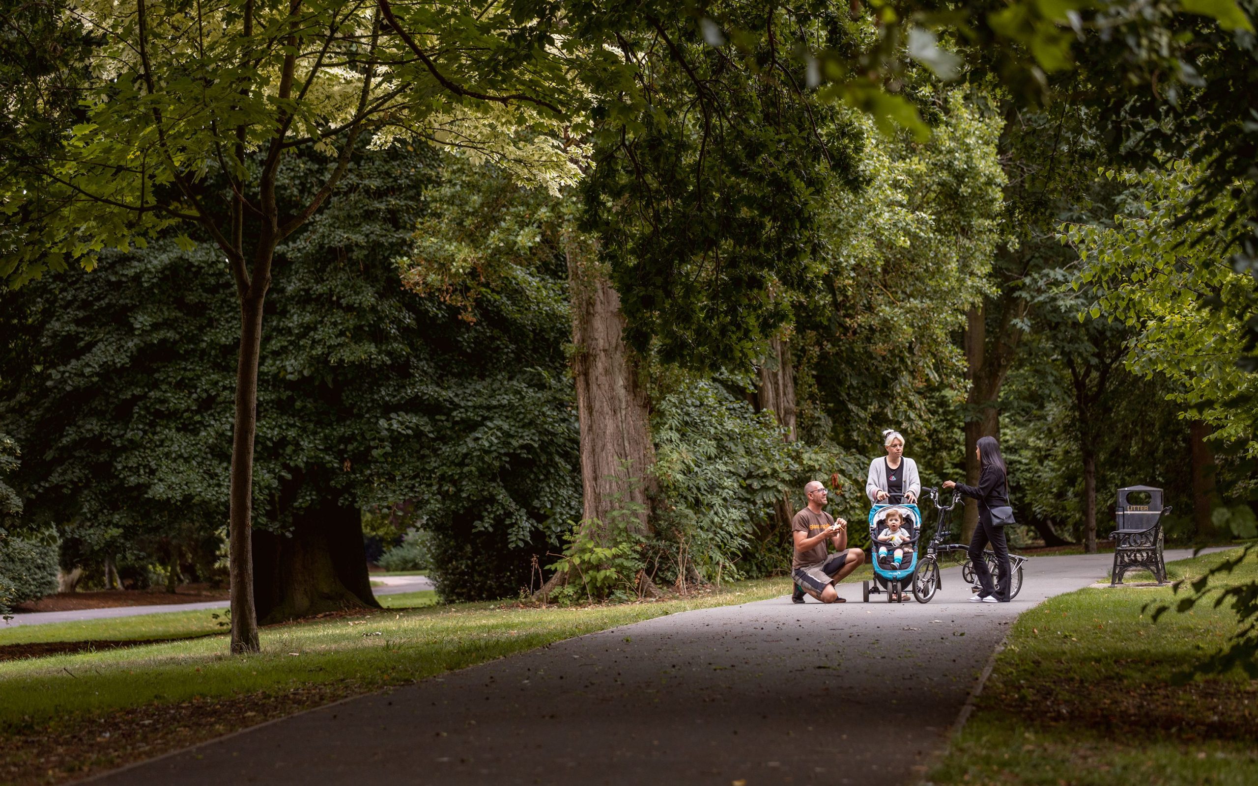 Two parents look after a small child in a pram, and talk to a woman using a bike on a path in Cycling and walking route in Leicester.
