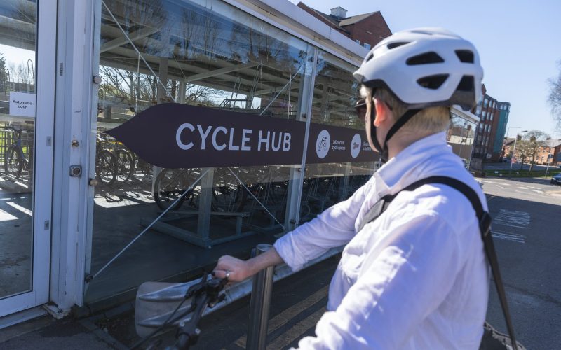 A person riding their bike in front of a Cycle Hub at a train station in Leicestershire. For cycling, commuting, Leicestershire businesses, new developments, communities.