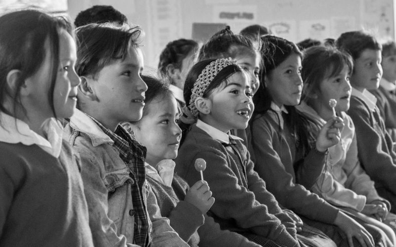 A line of young schoolchildren in uniform listening during an assembly. Some of the children are holding lollipops - for schools Active Travel Calendar